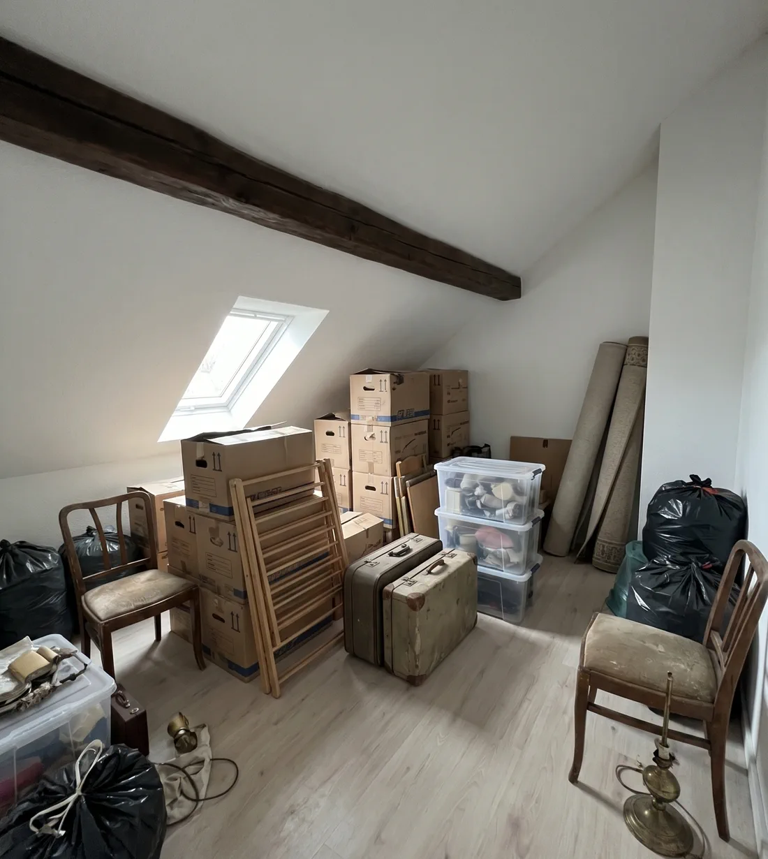 Beispieldarstellung: Dachgeschosszimmer mit Holzbalken vor der Räumung – Umzugskartons, Koffer, Stühle und Restmüll.