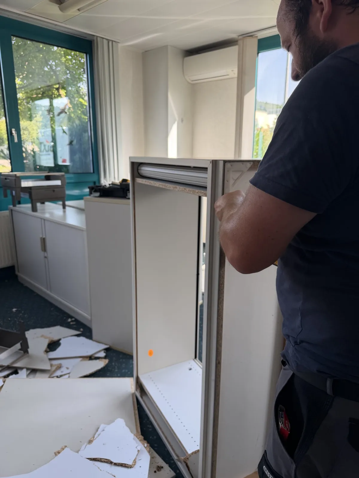 Mitarbeiter demontiert einen Rollladenschrank bei einer Büroräumung – Schränke werden vor Ort in Einzelteile zerlegt