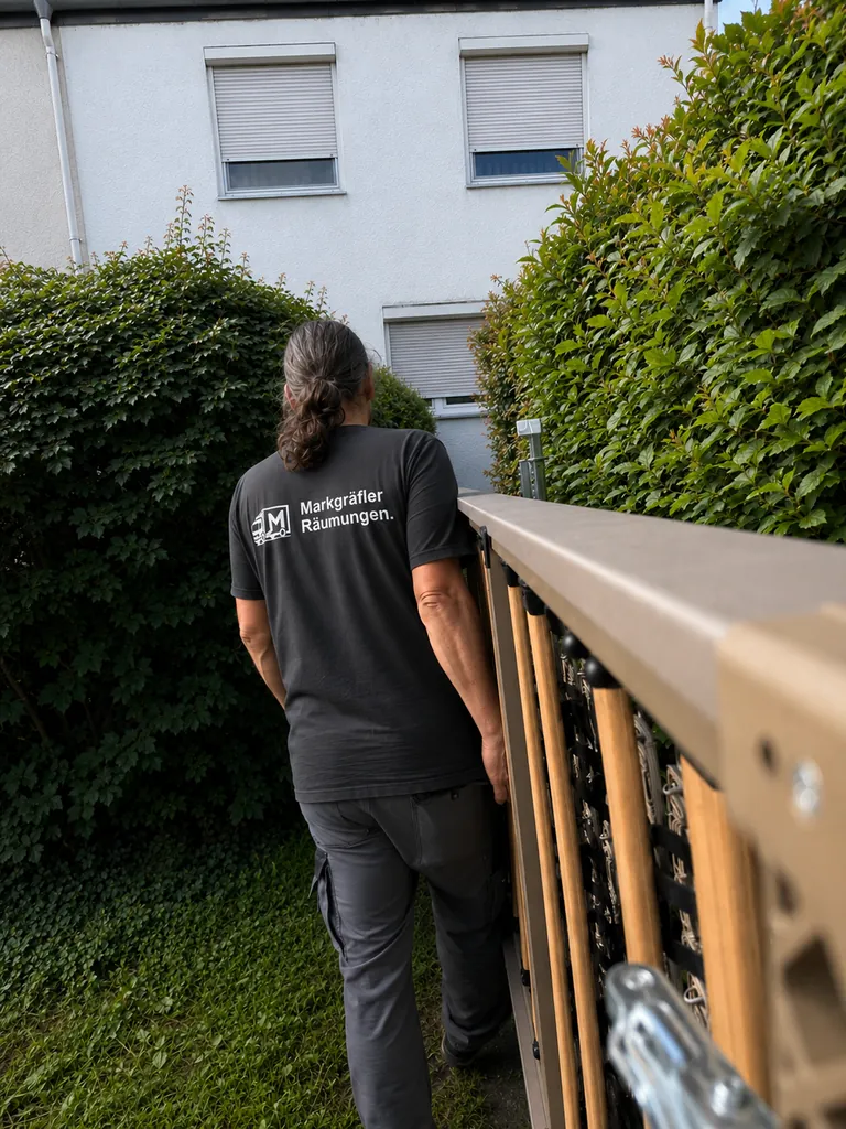 Mitarbeiter von Markgräfler Räumungen trägt einen Lattenrost durch ein Gartentor zum Transporter.